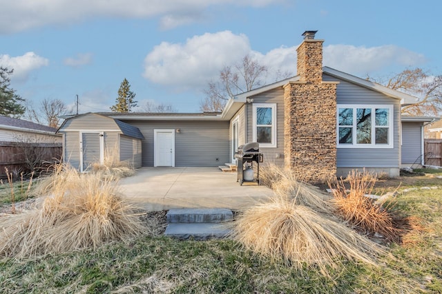 exterior space featuring an outbuilding, fence, a shed, a chimney, and a patio area