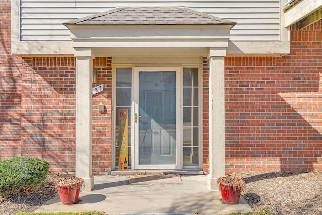 property entrance featuring brick siding and a shingled roof