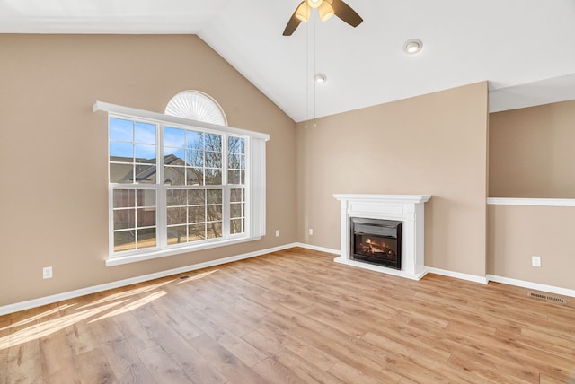 unfurnished living room featuring visible vents, vaulted ceiling, wood finished floors, a glass covered fireplace, and a ceiling fan