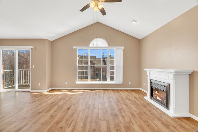 unfurnished living room featuring light wood finished floors, baseboards, ceiling fan, vaulted ceiling, and a glass covered fireplace