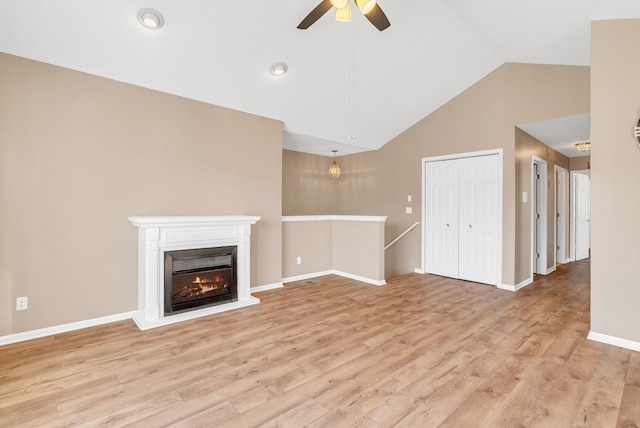 unfurnished living room with a ceiling fan, baseboards, light wood finished floors, lofted ceiling, and a glass covered fireplace