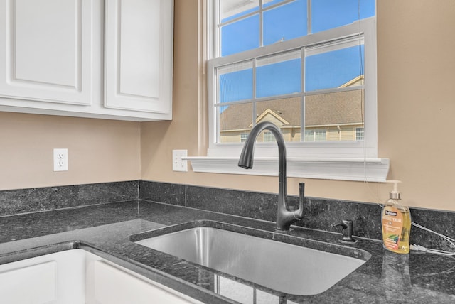 details with dark stone countertops, white cabinets, and a sink