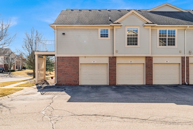 view of property exterior with community garages, brick siding, and a shingled roof