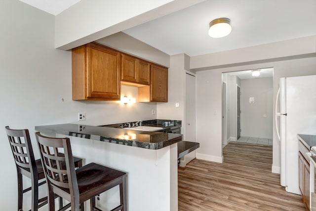 kitchen with dark countertops, a breakfast bar area, light wood-type flooring, a peninsula, and a sink