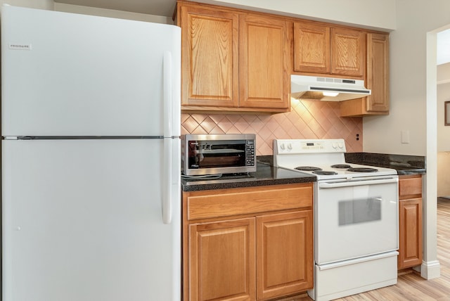 kitchen featuring under cabinet range hood, dark stone counters, decorative backsplash, light wood-style flooring, and white appliances