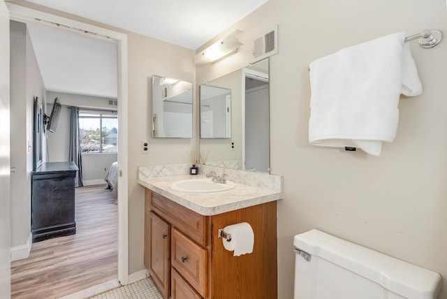 ensuite bathroom featuring visible vents, toilet, wood finished floors, baseboards, and vanity