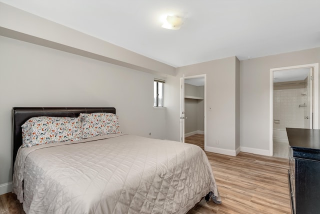 bedroom with light wood-style flooring, ensuite bathroom, and baseboards