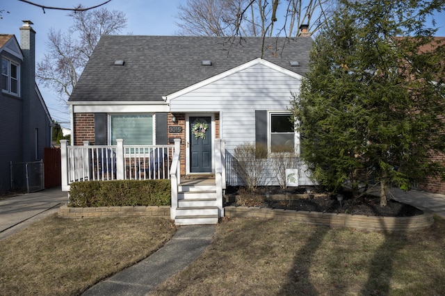 view of front of house featuring a porch, a front lawn, brick siding, and a shingled roof