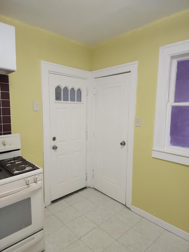 kitchen featuring light tile patterned floors, baseboards, and white gas range oven