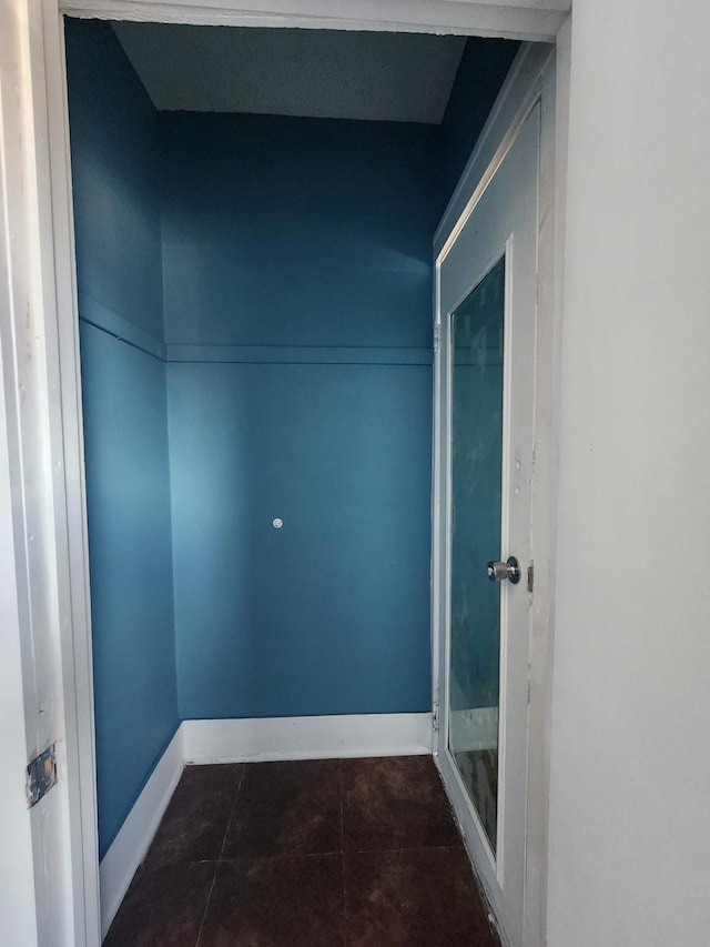 hallway featuring dark tile patterned floors and baseboards