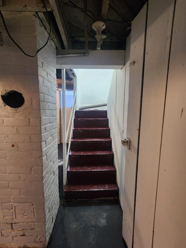stairs featuring brick wall and unfinished concrete flooring