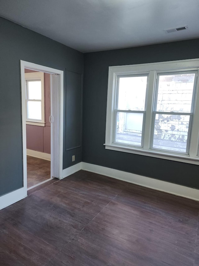 empty room with dark wood-type flooring, baseboards, and visible vents