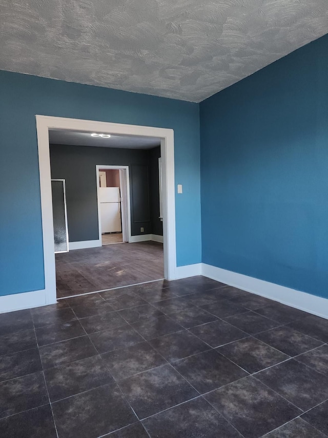 tiled empty room featuring baseboards and a textured ceiling