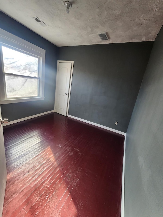 spare room with visible vents, baseboards, and dark wood-style flooring
