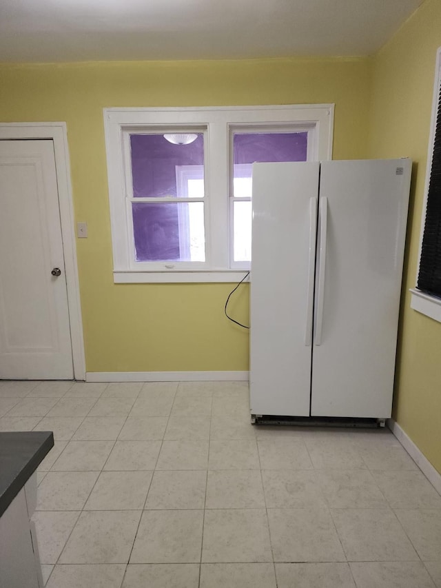 kitchen with light tile patterned floors, baseboards, dark countertops, and freestanding refrigerator