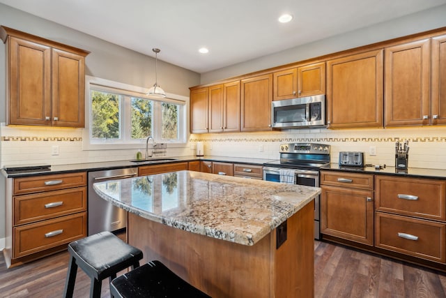 kitchen featuring dark stone countertops, appliances with stainless steel finishes, a kitchen breakfast bar, dark wood-style floors, and a sink