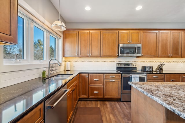 kitchen with a sink, brown cabinets, appliances with stainless steel finishes, and dark stone countertops