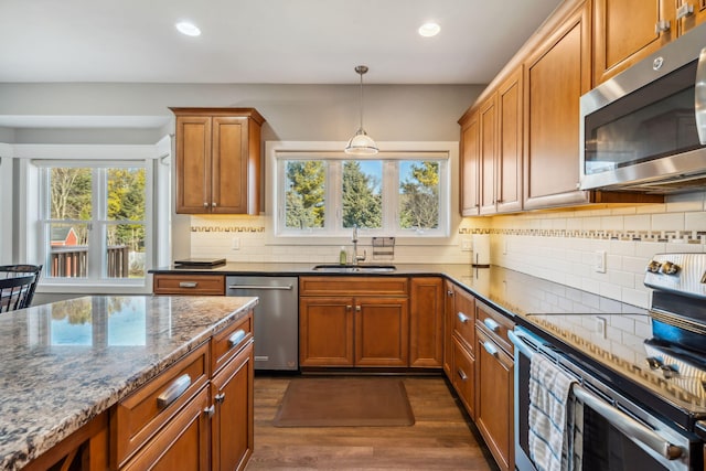 kitchen featuring backsplash, dark wood-type flooring, dark stone counters, appliances with stainless steel finishes, and a sink