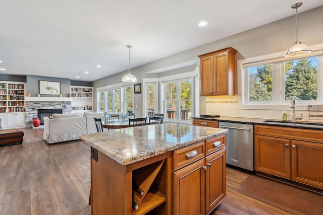 kitchen with brown cabinetry, a fireplace, a sink, dark wood-type flooring, and stainless steel dishwasher