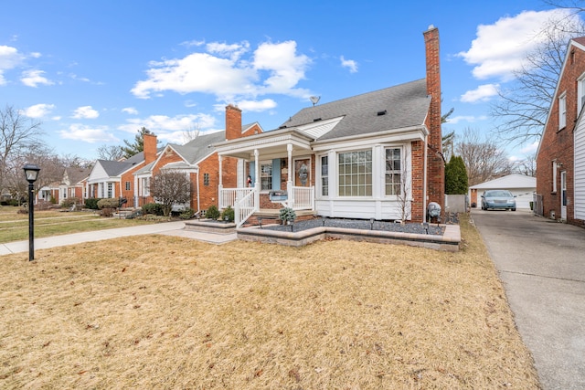 bungalow-style house featuring an outbuilding, covered porch, a chimney, a front lawn, and brick siding