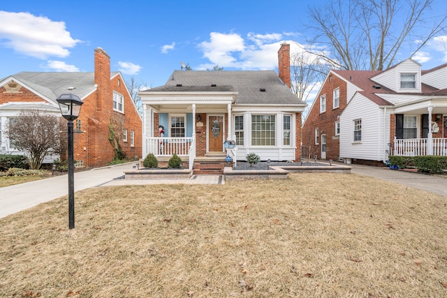 view of front of home featuring brick siding, covered porch, a chimney, and a front lawn