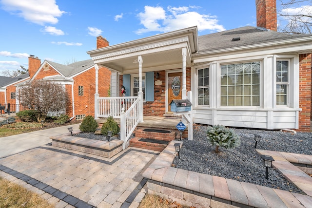 view of front of house featuring brick siding, covered porch, a chimney, and a shingled roof