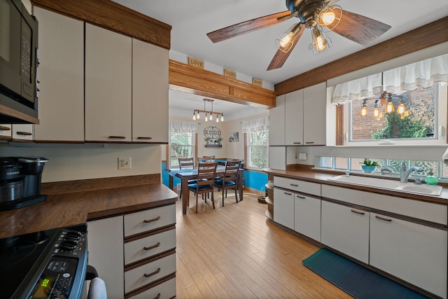 kitchen featuring black microwave, light wood-type flooring, electric stove, white cabinetry, and a sink