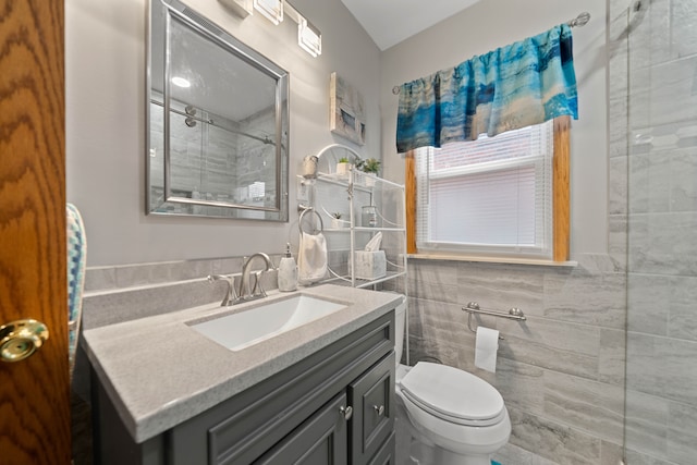 bathroom with vanity, tile walls, toilet, and a tile shower