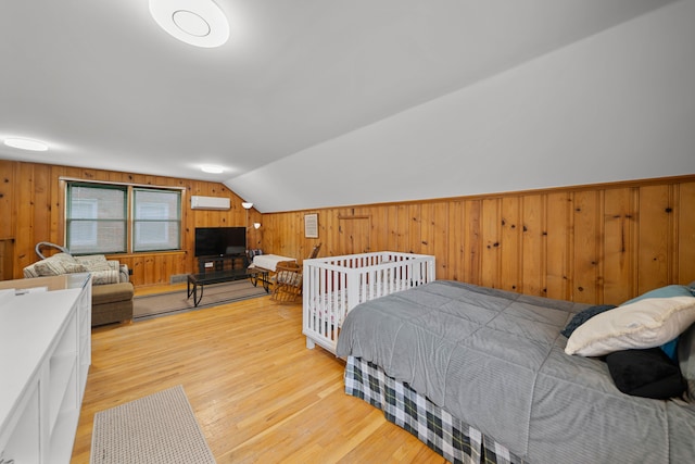 bedroom with wooden walls, a wall mounted air conditioner, light wood-style floors, and vaulted ceiling