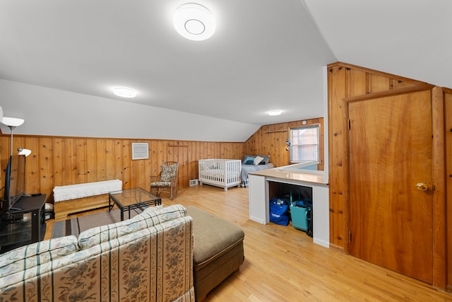 living room featuring light wood finished floors, wooden walls, and vaulted ceiling