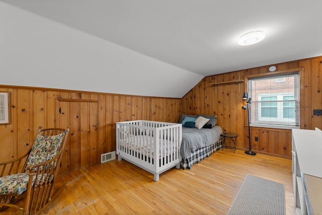 bedroom featuring visible vents, light wood-style flooring, wooden walls, and vaulted ceiling