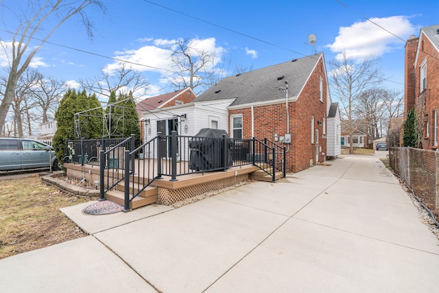 back of property with brick siding, a shingled roof, a wooden deck, and fence