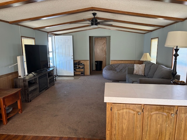 living room featuring a textured ceiling, vaulted ceiling with beams, ceiling fan, wainscoting, and dark colored carpet