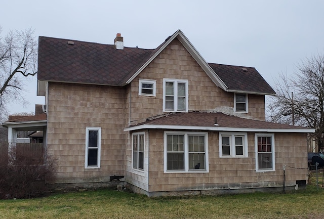 back of property featuring a chimney, a yard, and roof with shingles