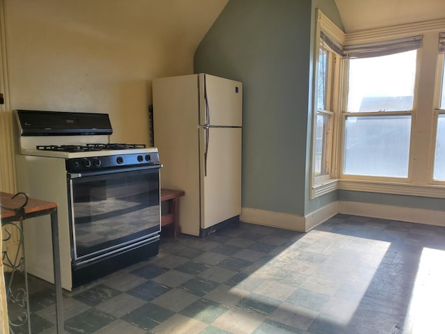 kitchen featuring baseboards, dark floors, lofted ceiling, freestanding refrigerator, and gas stove