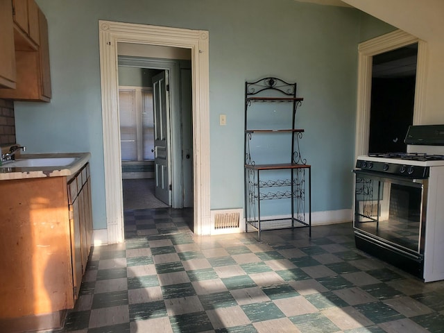 kitchen featuring visible vents, a sink, light countertops, black gas range, and dark floors