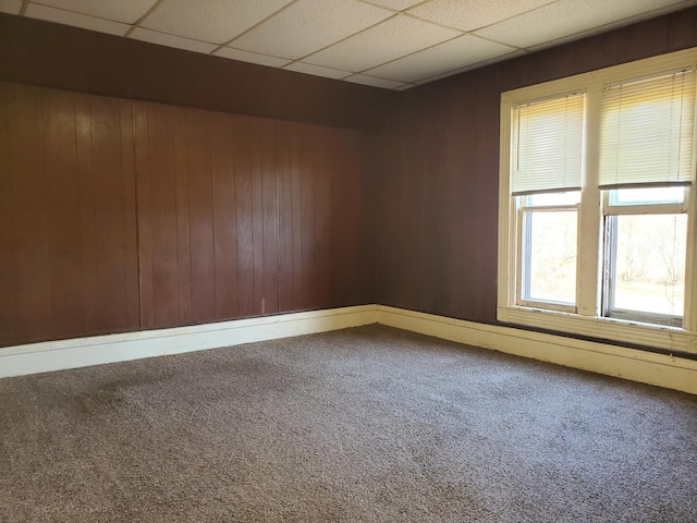 carpeted spare room with a paneled ceiling and wood walls