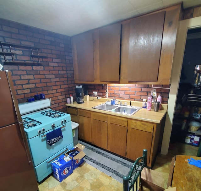 kitchen featuring white gas stove, a sink, freestanding refrigerator, brick wall, and light countertops