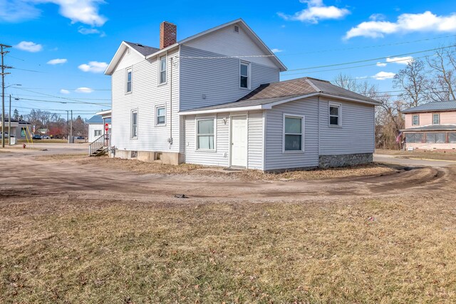 back of property with entry steps, a lawn, driveway, and a chimney