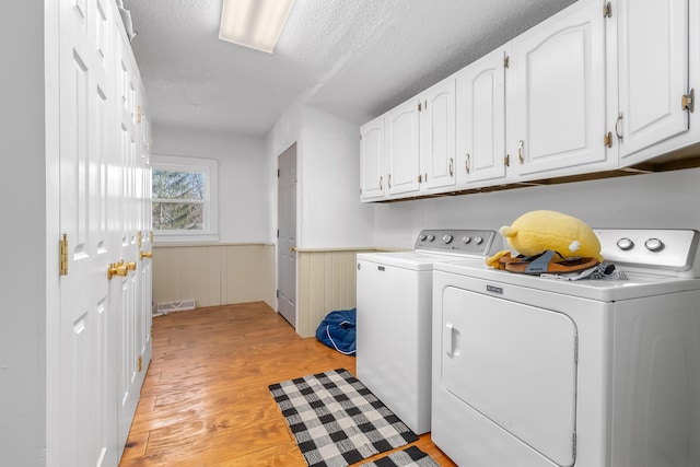 laundry area featuring visible vents, a wainscoted wall, light wood-type flooring, cabinet space, and separate washer and dryer