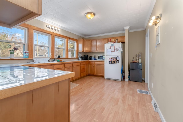 kitchen with tile counters, visible vents, freestanding refrigerator, and light wood-type flooring