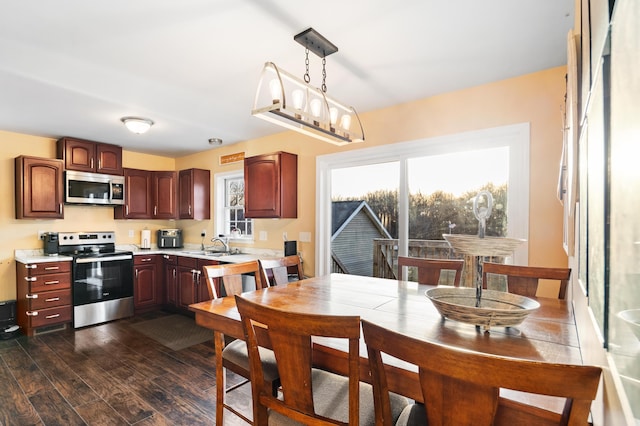 kitchen featuring dark wood finished floors, light countertops, hanging light fixtures, stainless steel appliances, and a sink