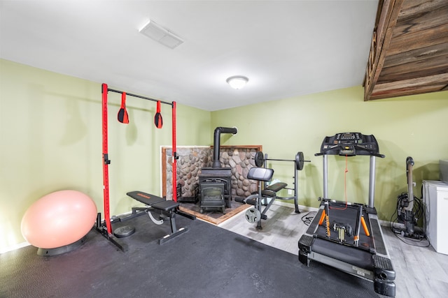 exercise area with visible vents, a wood stove, baseboards, and wood finished floors