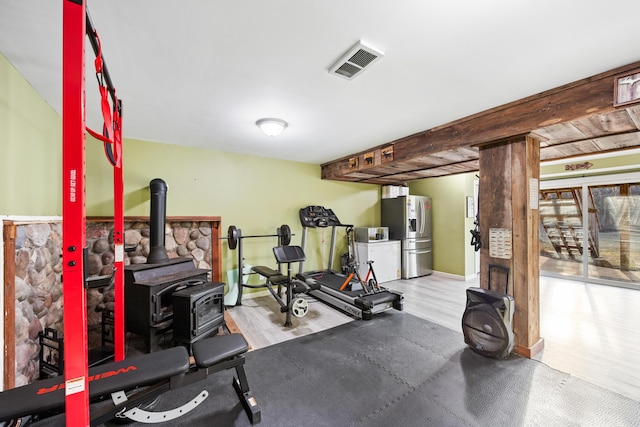 exercise room with a wood stove, wood finished floors, visible vents, and baseboards