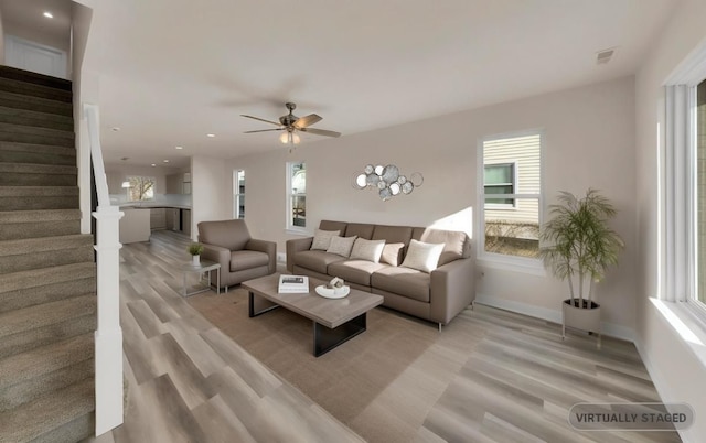 living area featuring light wood finished floors, visible vents, baseboards, ceiling fan, and stairway