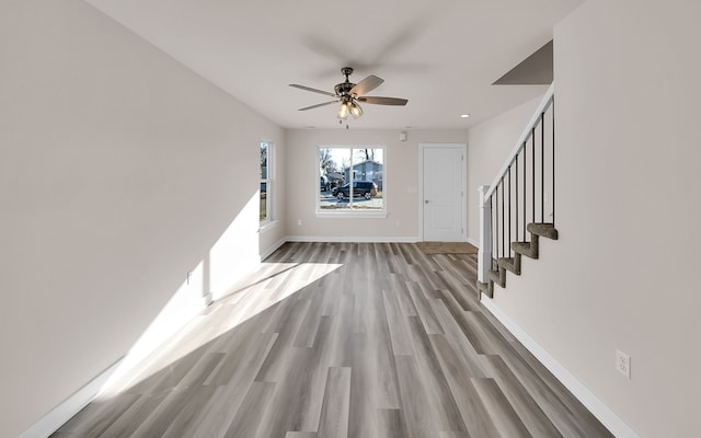 unfurnished living room with stairway, wood finished floors, baseboards, and ceiling fan