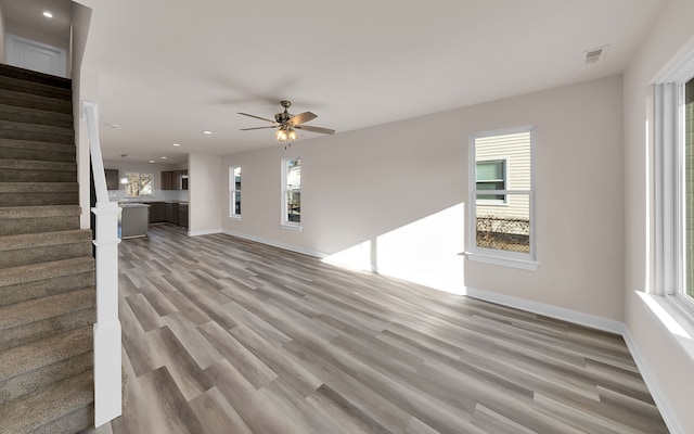 unfurnished living room featuring light wood-type flooring, visible vents, baseboards, and stairs