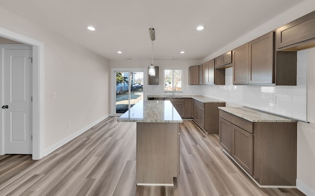 kitchen with light stone counters, light wood-style floors, baseboards, and backsplash