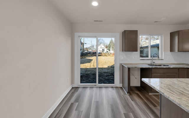 kitchen with wood finished floors, baseboards, light stone countertops, visible vents, and a sink