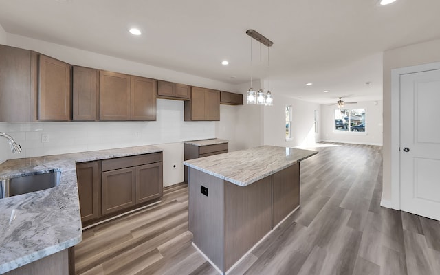 kitchen with light wood-style flooring, light stone counters, tasteful backsplash, and a sink